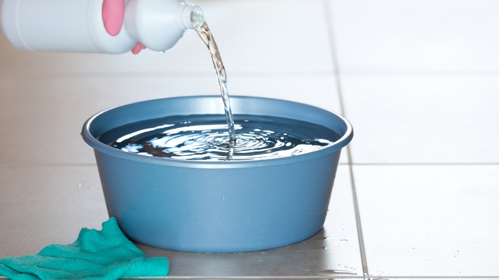 A light blue basin being filled with water from a white bottle.