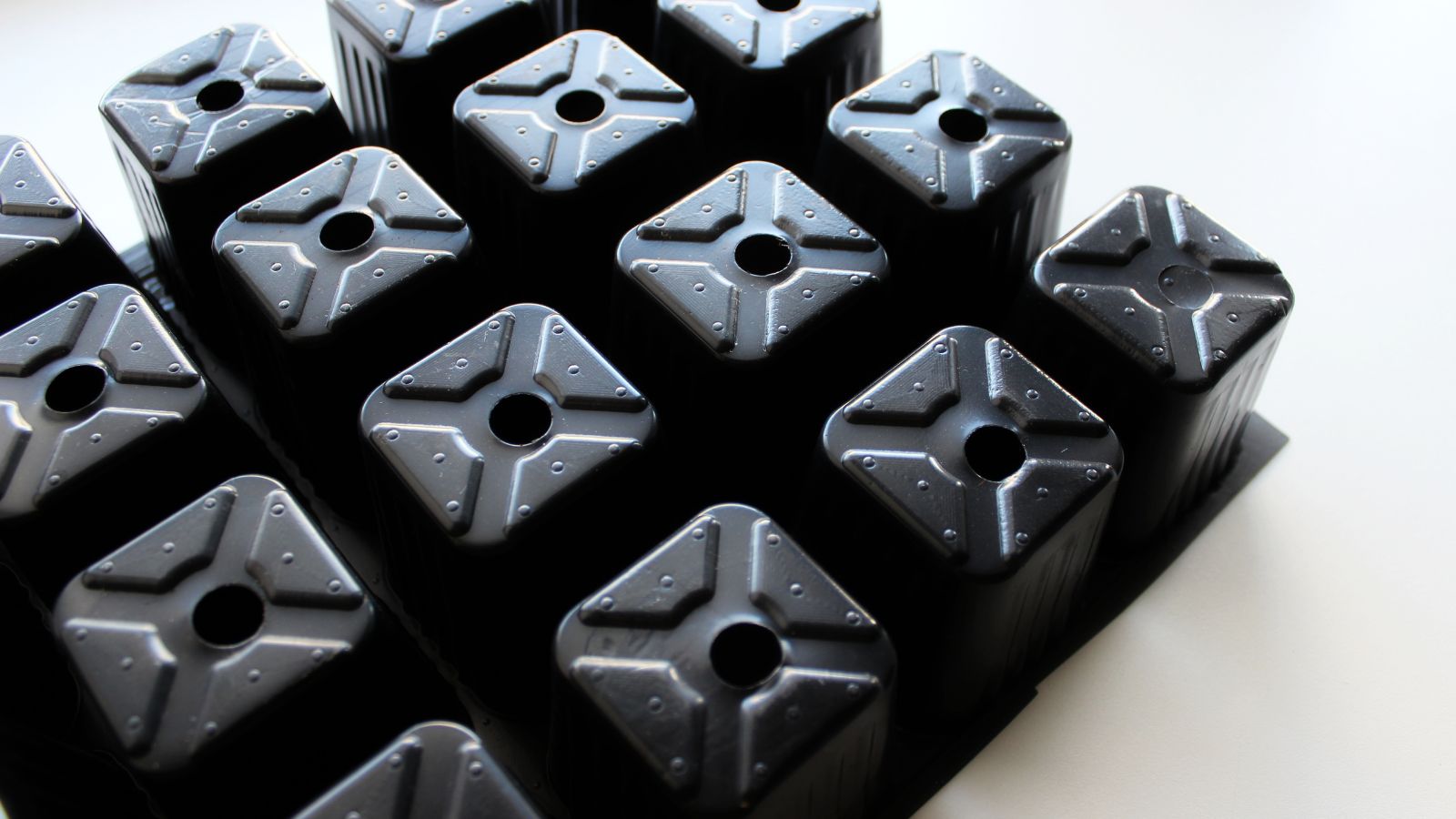 A black seed tray with holes turned upside down placed on a pure white surface.